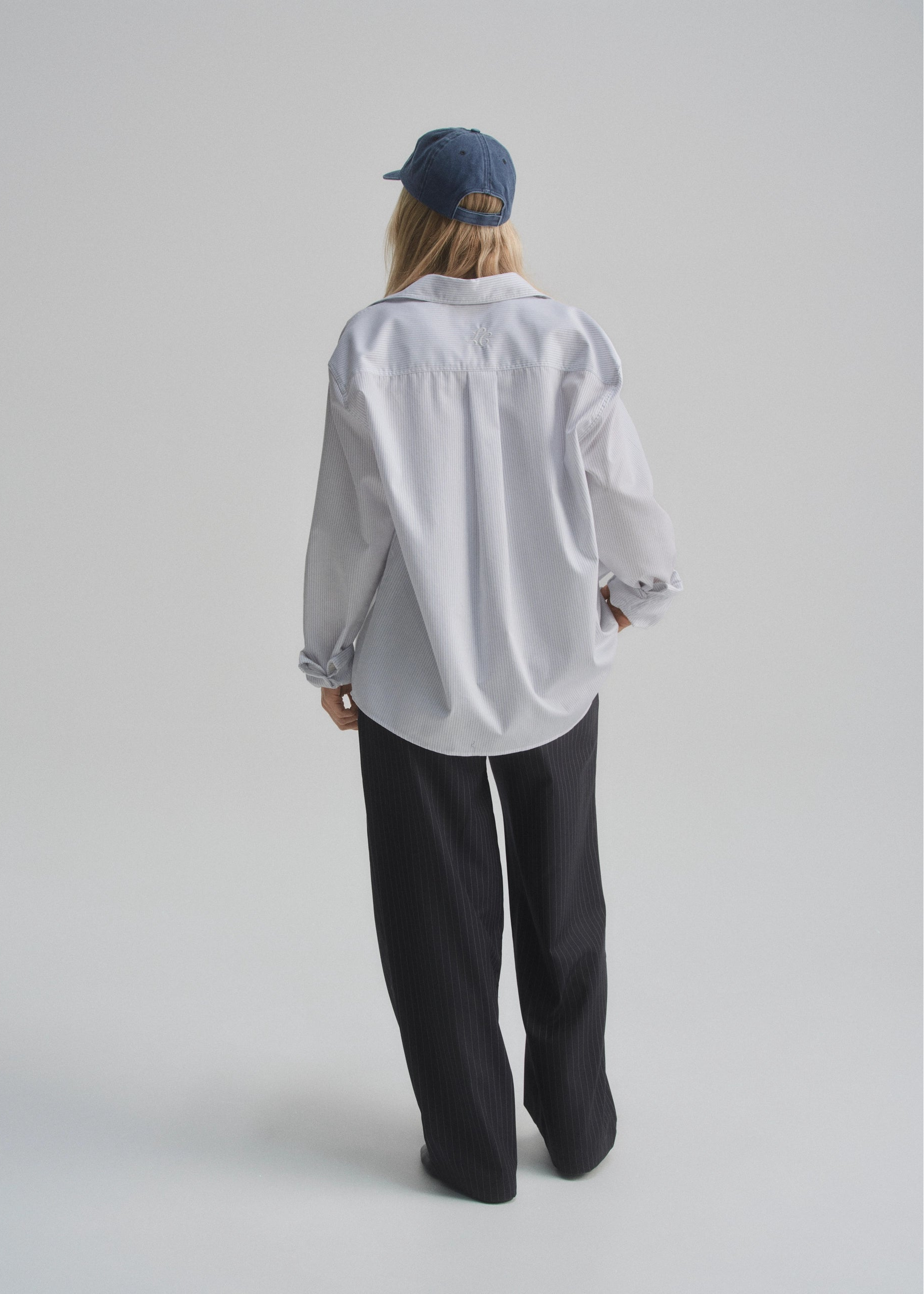 Person wearing a white pinstripe oversized shirt and black pants on a plain background