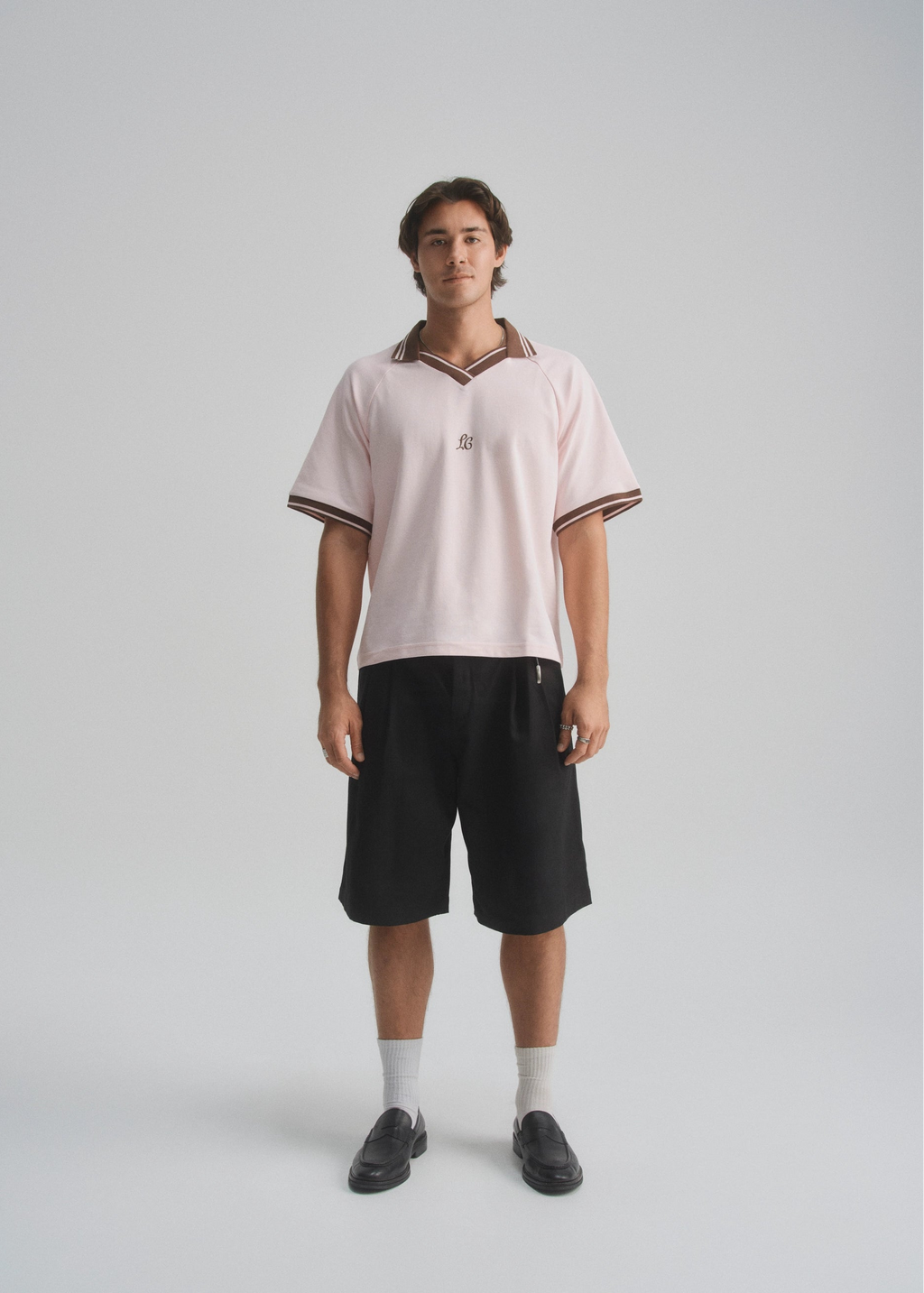 Person wearing a light pink polo shirt and black shorts on a white background