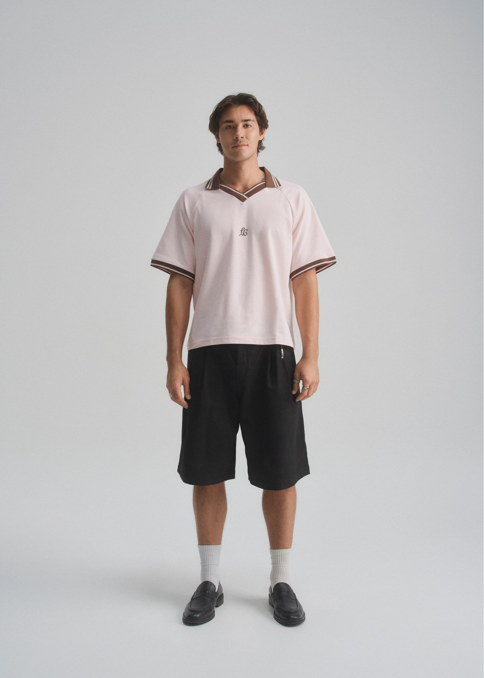 Person wearing a light pink polo shirt and black shorts on a white background