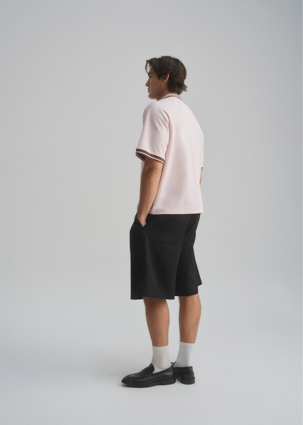 Person wearing a light pink shirt with dark brown trim and black shorts on a white background