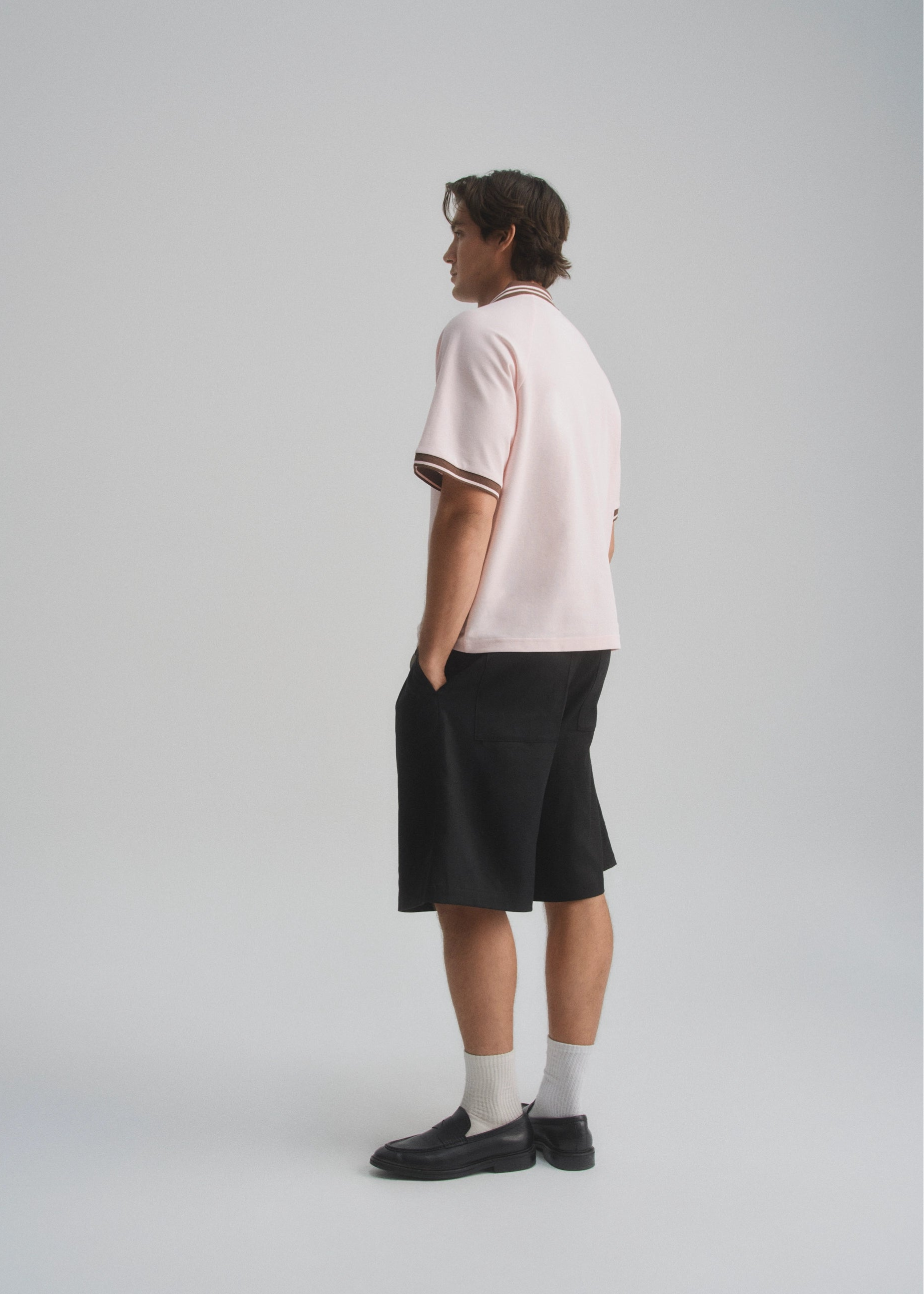 Person wearing a light pink shirt with dark brown trim and black shorts on a white background