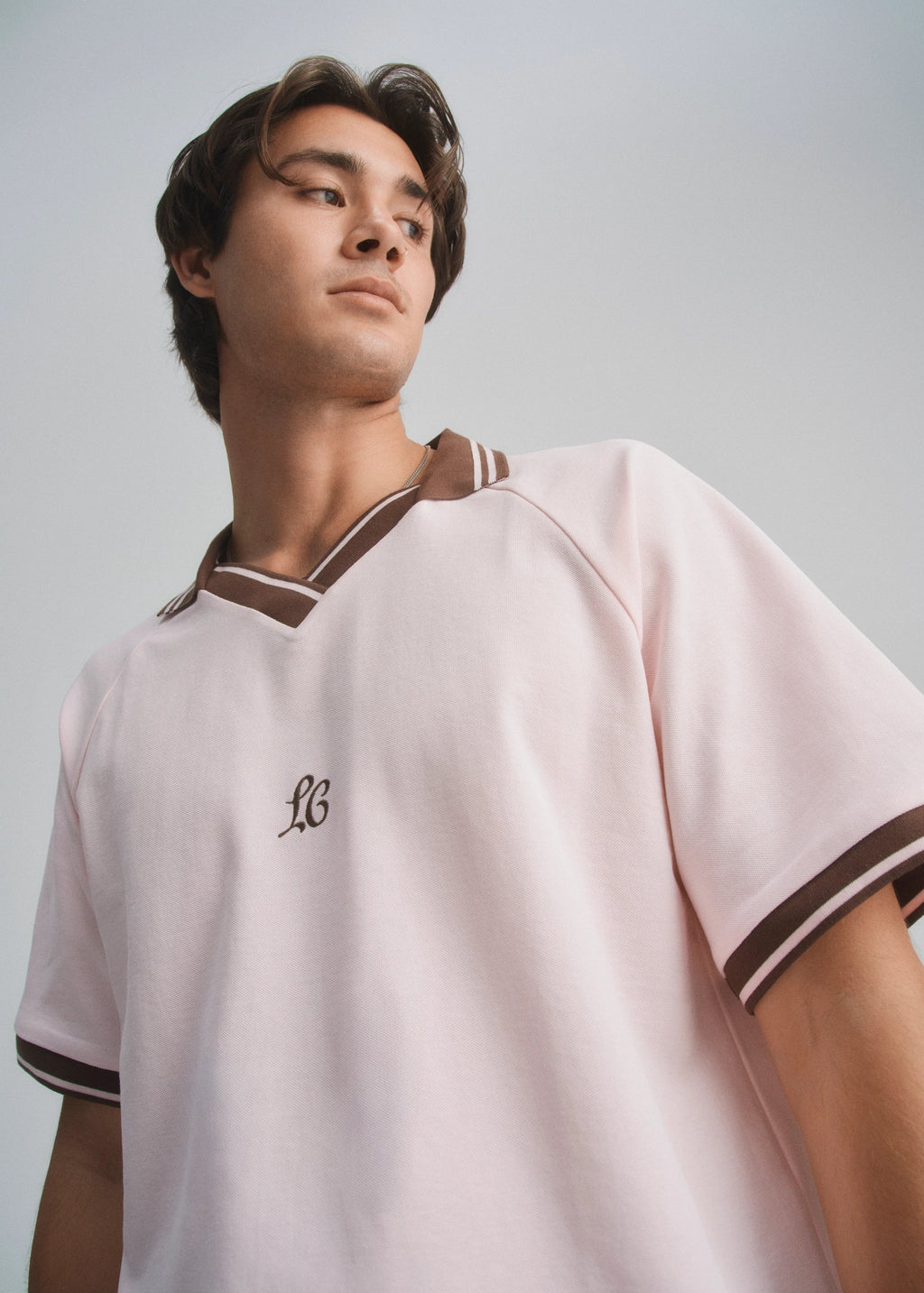 Person wearing a light pink sports jersey with brown accents on a plain background