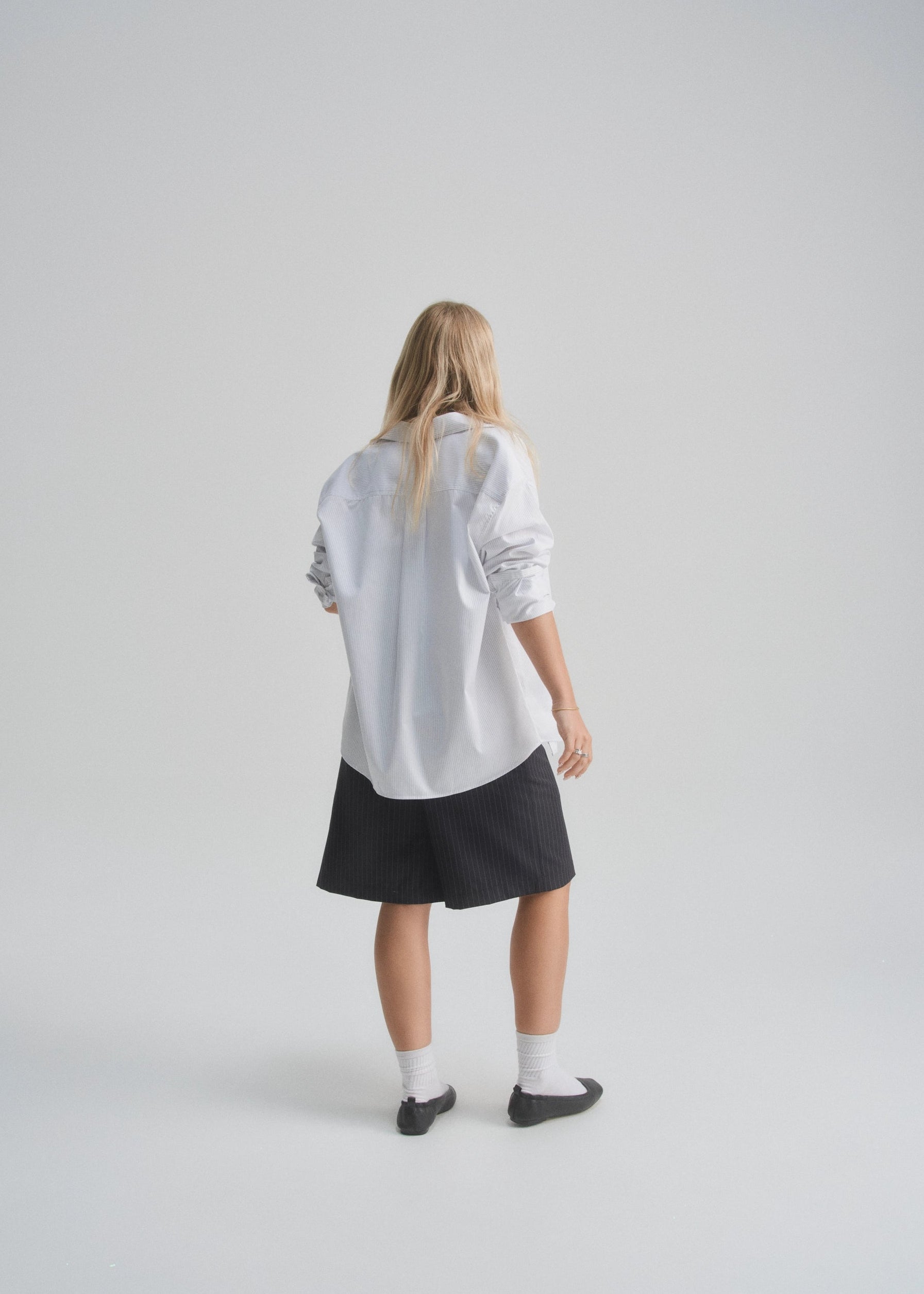 Person wearing a white shirt and dark navy pinstripe shorts on a plain background