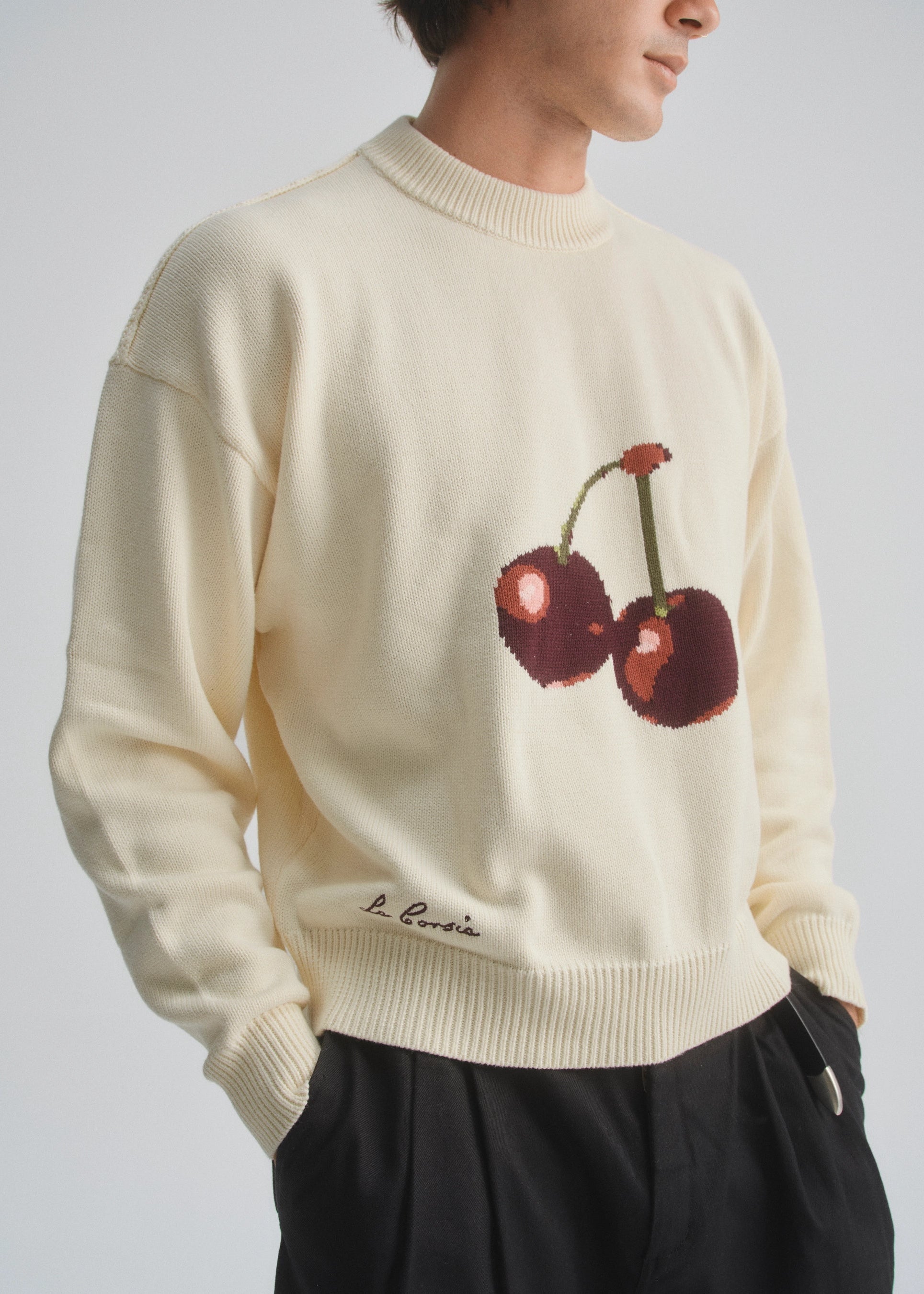 Person wearing a cream sweater with cherry design on a plain background