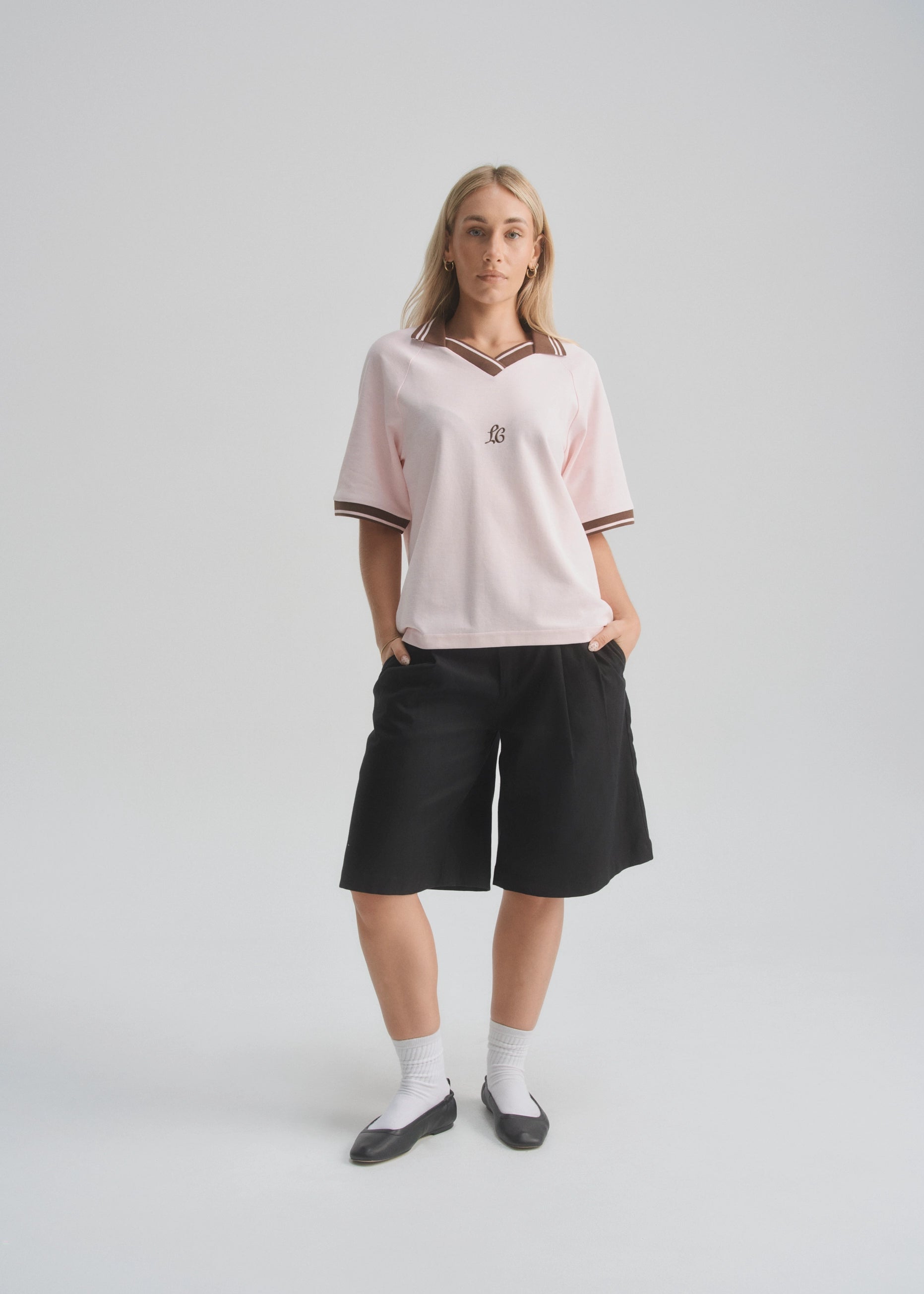 Person wearing a light pink oversized shirt and black shorts on a white background
