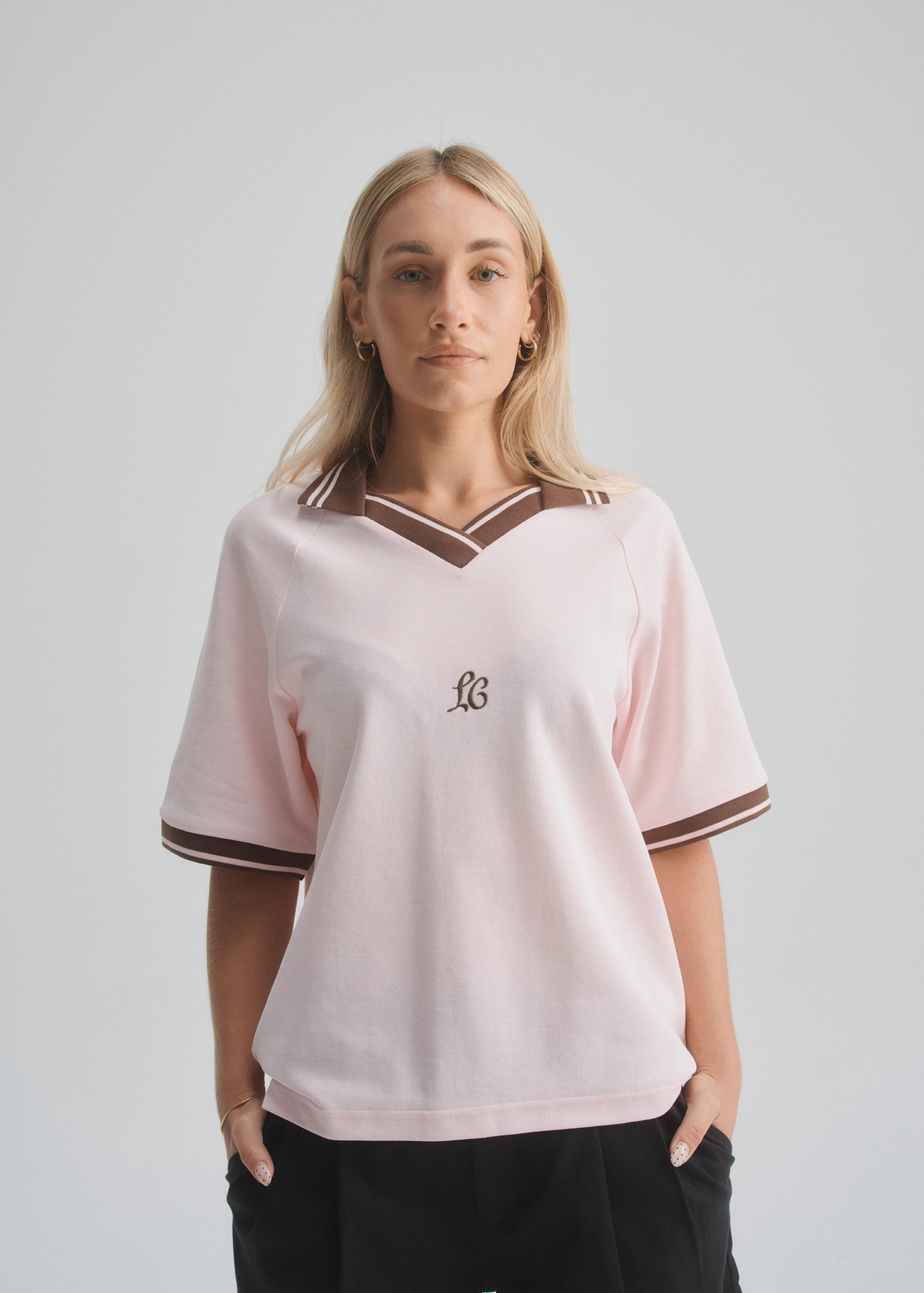 Woman wearing a light pink jersey with a logo on a plain background