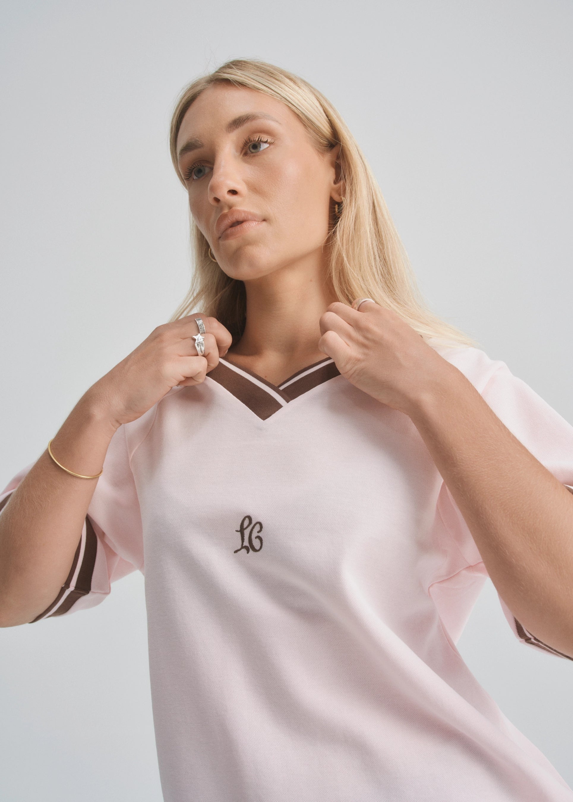 Woman wearing a light pink sports jersey with a logo on a plain background