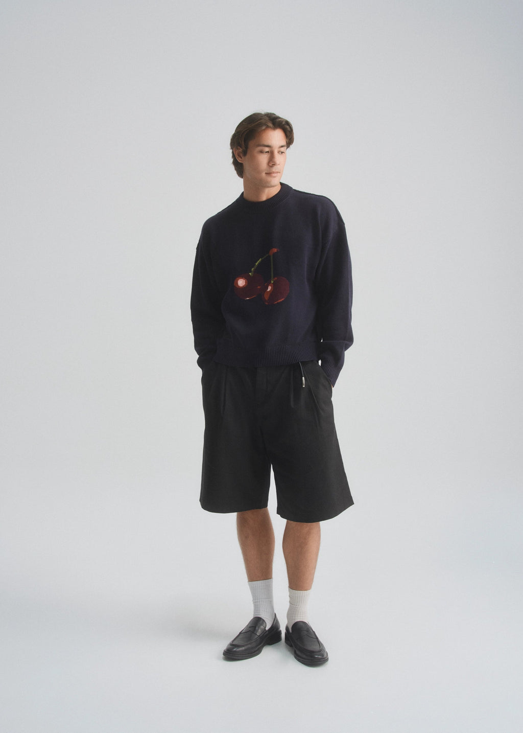 Person wearing a dark navy sweater with cherry design and black shorts on a white background