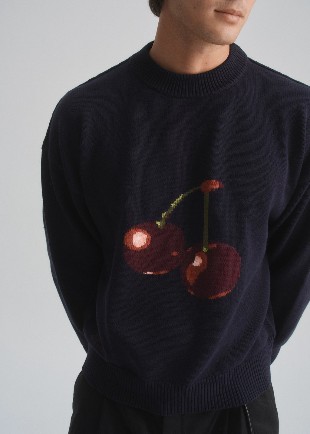Navy sweater with cherry design worn by a person on a plain background