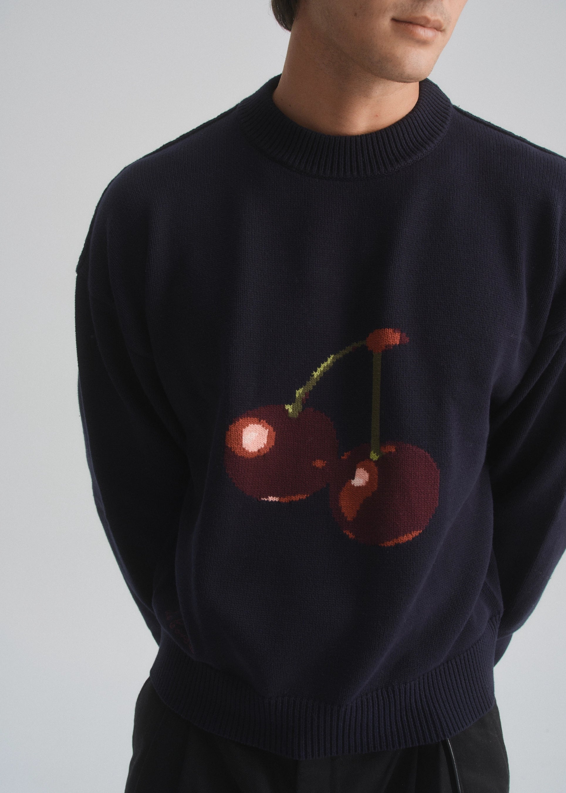 Navy sweater with cherry design worn by a person on a plain background