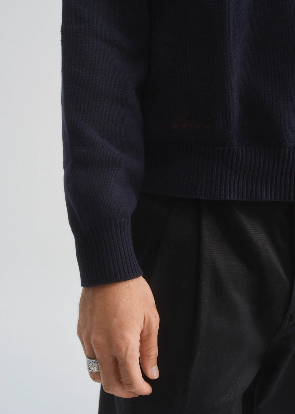 Navy sweater with a brand logo worn by a person on a light gray background