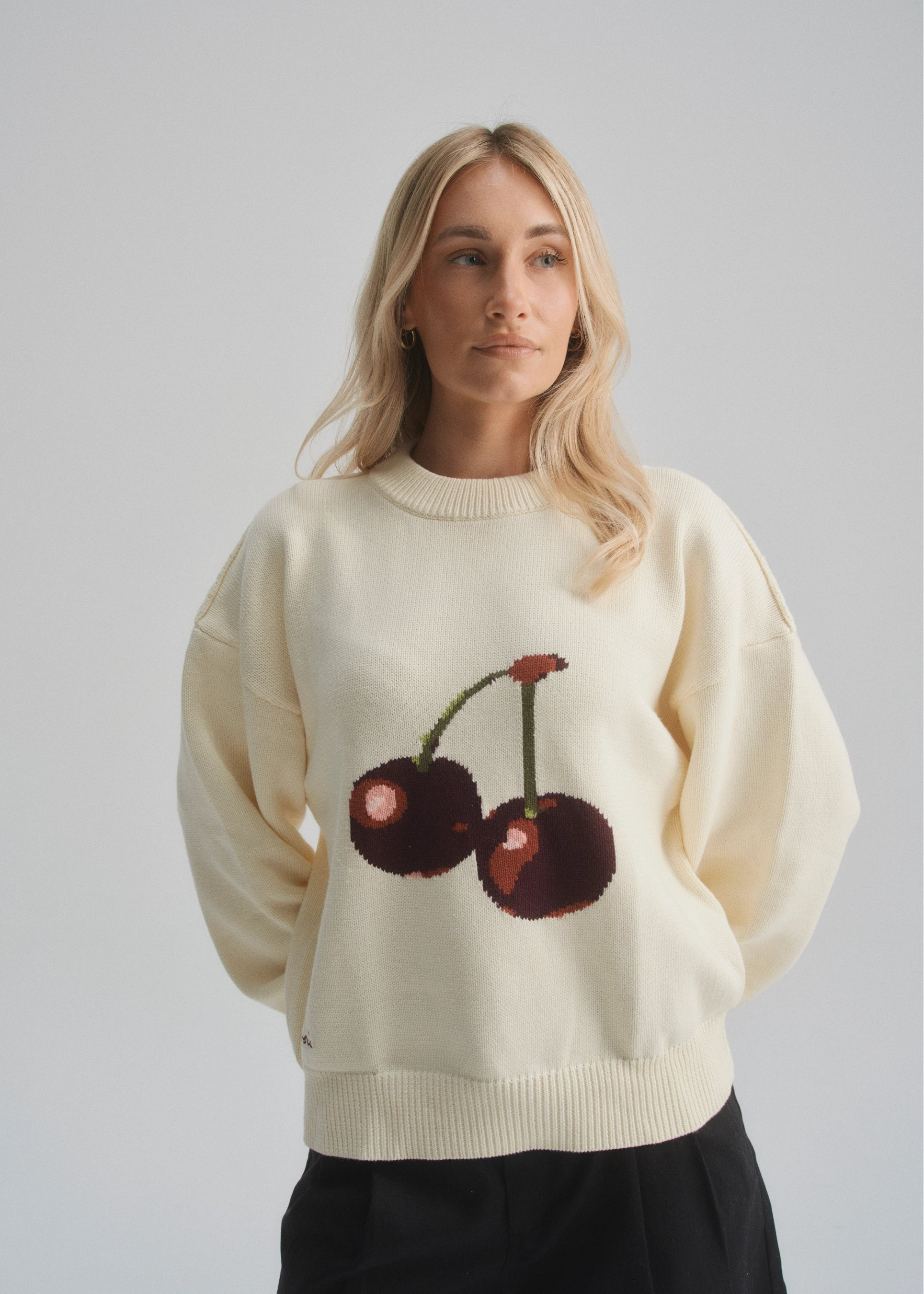 Person wearing a cream sweater with cherry design on a plain background
