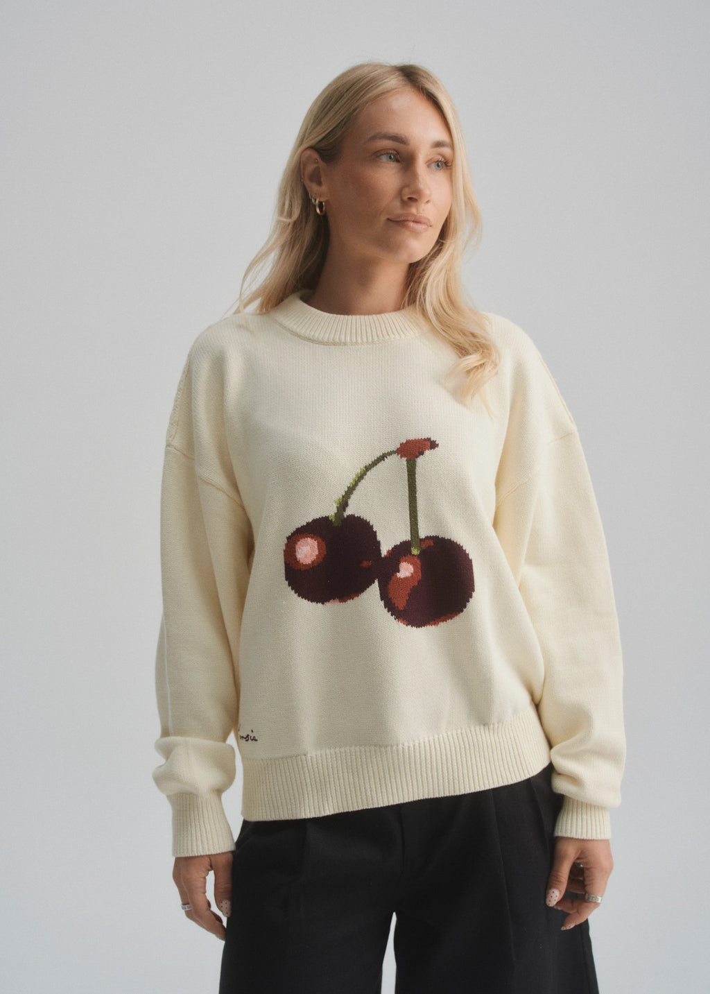 Woman wearing a cream sweater with cherry design against a plain background