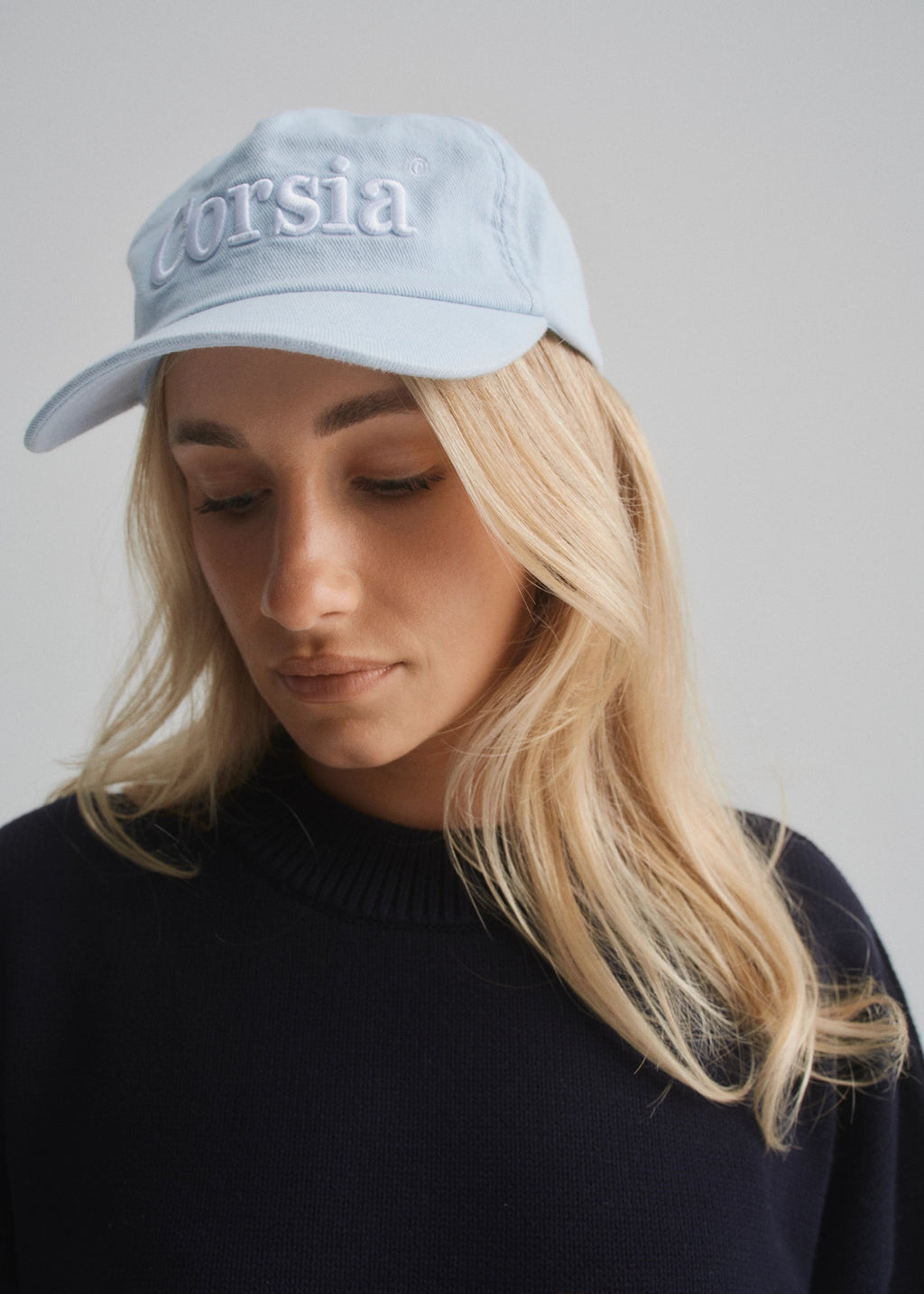 Person wearing a light blue cap with 'Corsia' text on a plain background