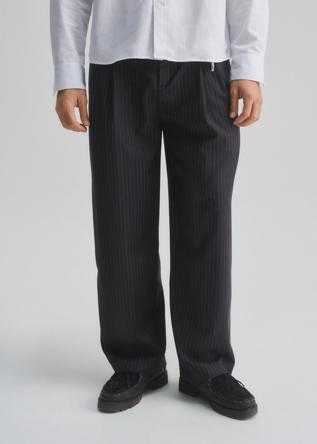 Person wearing dark navy pinstripe pants and a light-colored shirt on a plain background