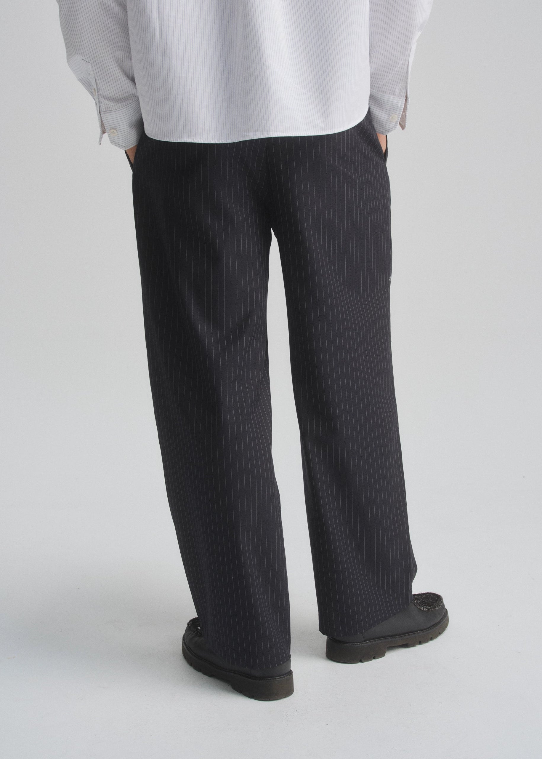 Person wearing black pinstripe pants and a light gray shirt on a white background