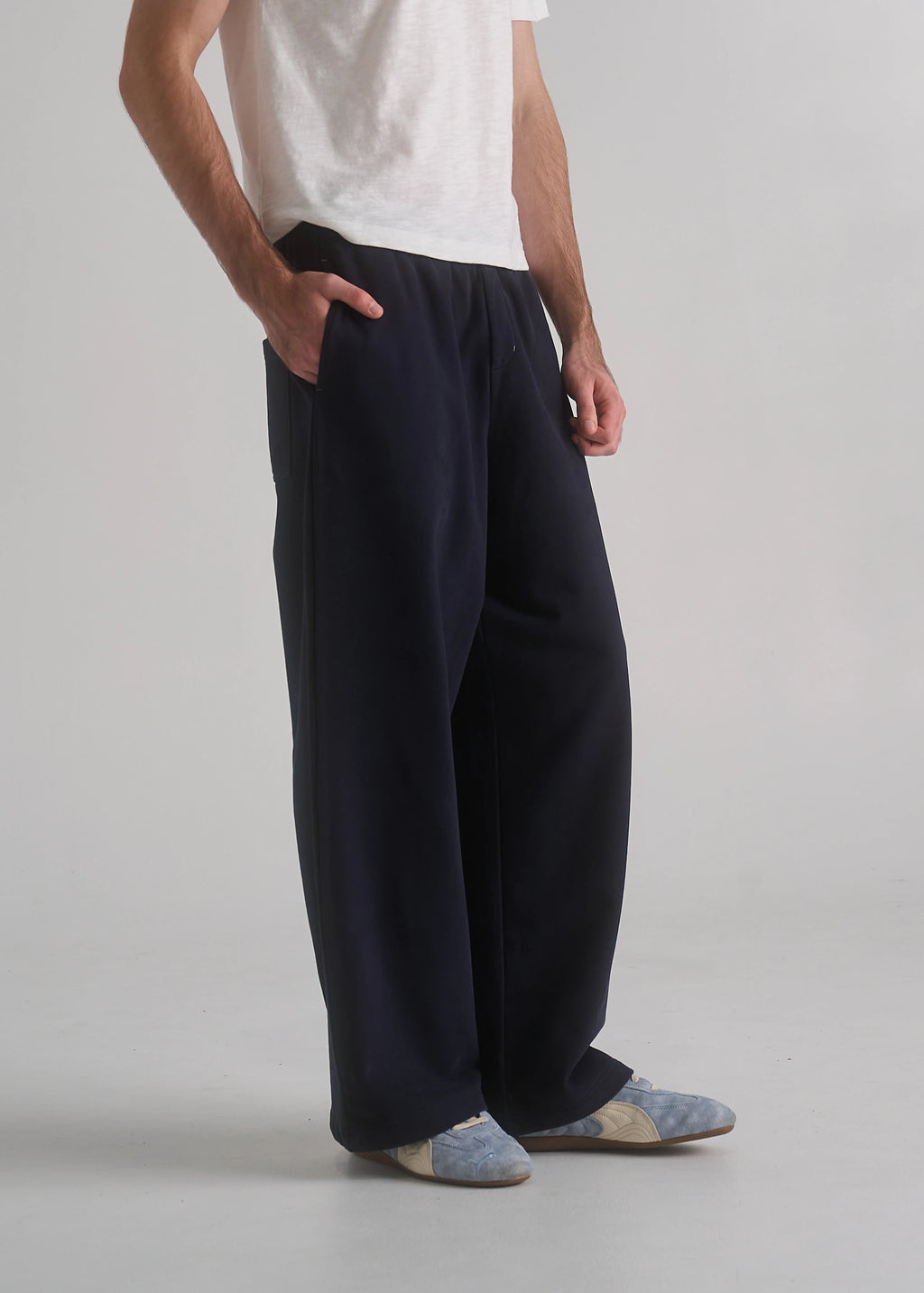 Person wearing navy pants and a white shirt on a plain background