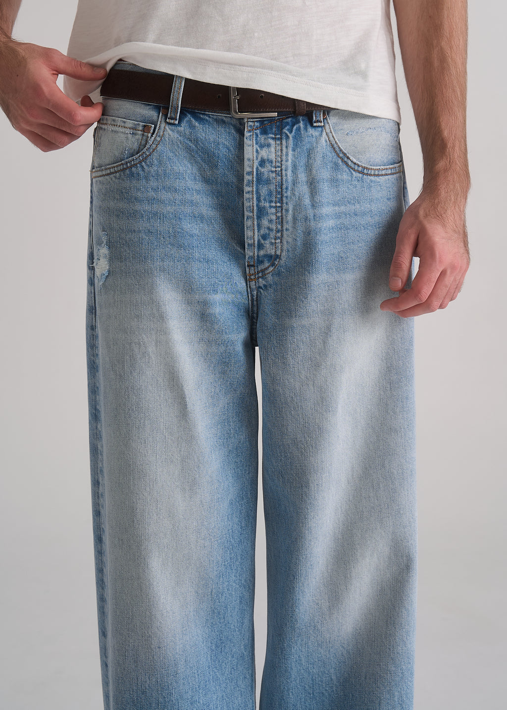 Person wearing light blue jeans and a white shirt on a plain background