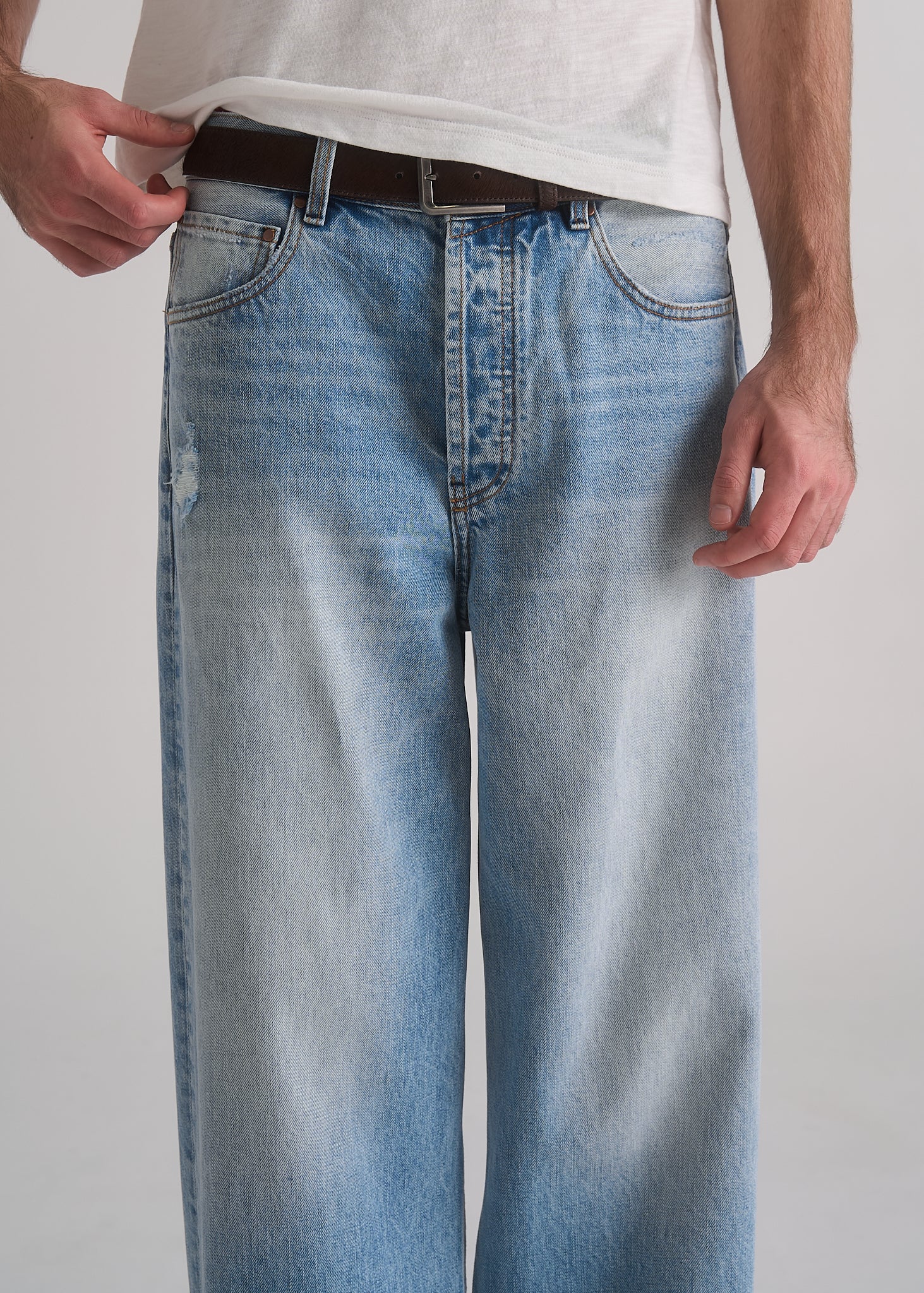 Person wearing light blue jeans and a white shirt on a plain background