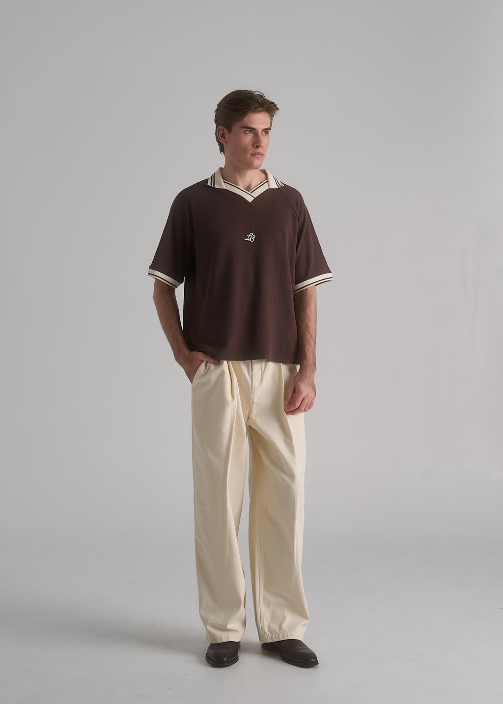Man wearing a brown polo shirt and beige pants on a gray background