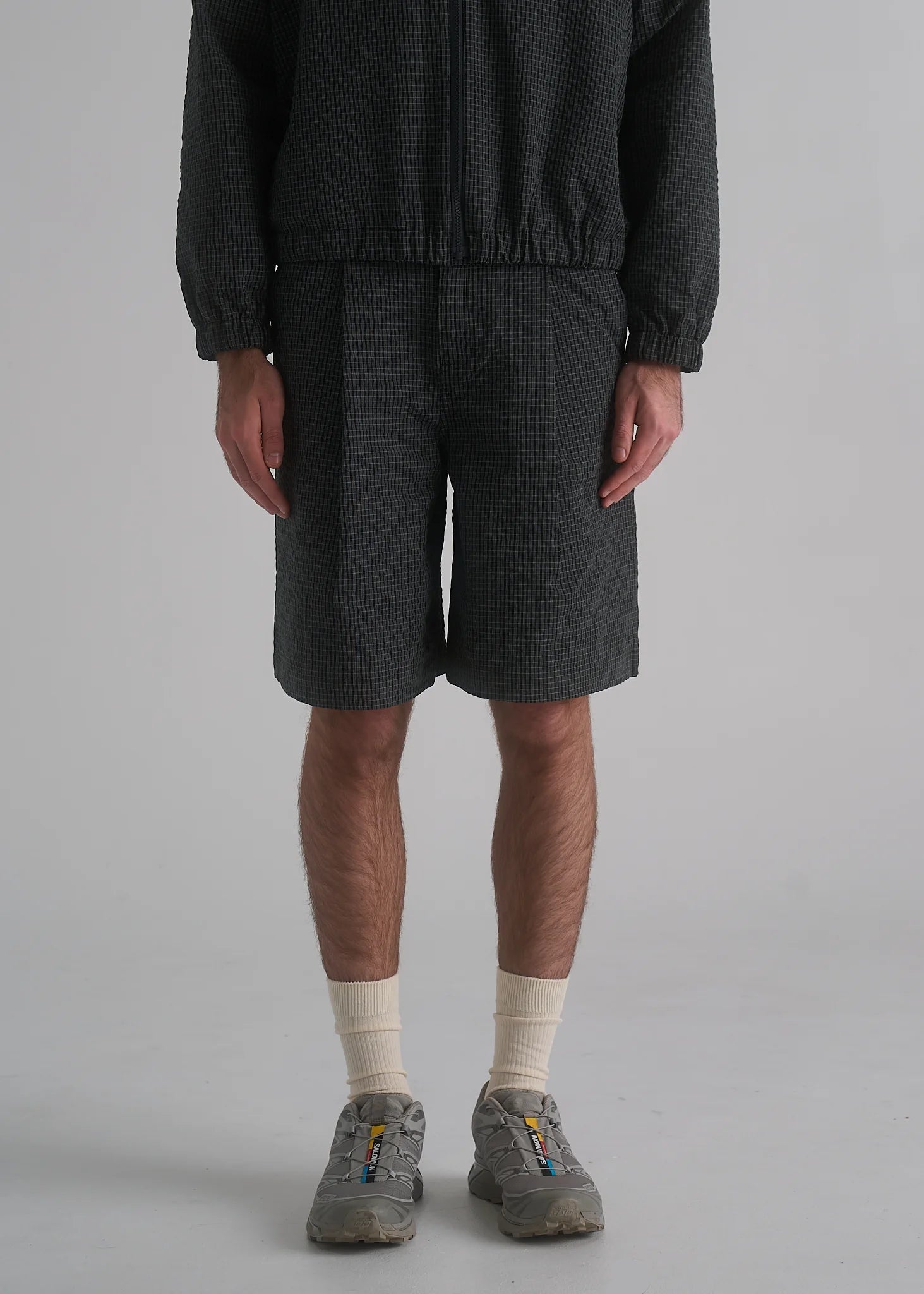 Person wearing dark shorts and a textured top on a plain background