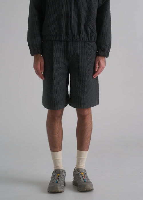 Person wearing dark shorts and a textured top on a plain background