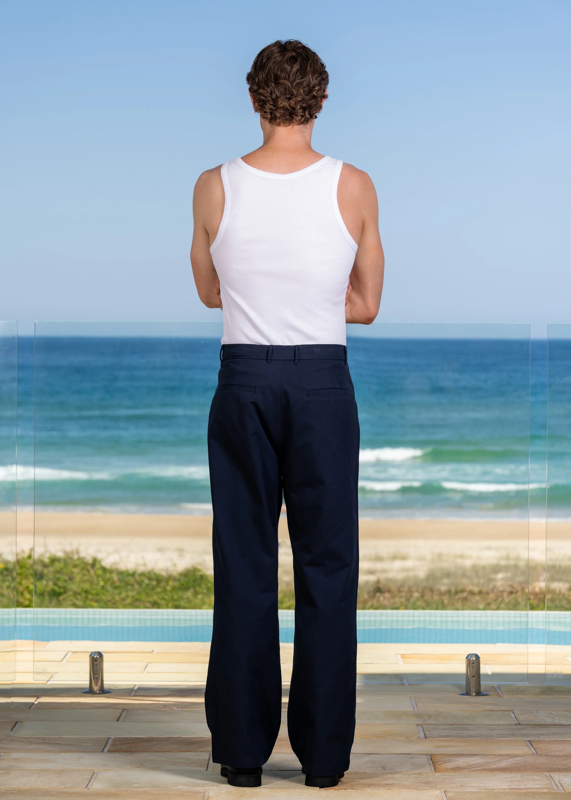 Back view of model in white ribbed tank top, scooped neckline, and classic fit, coastal fashion.