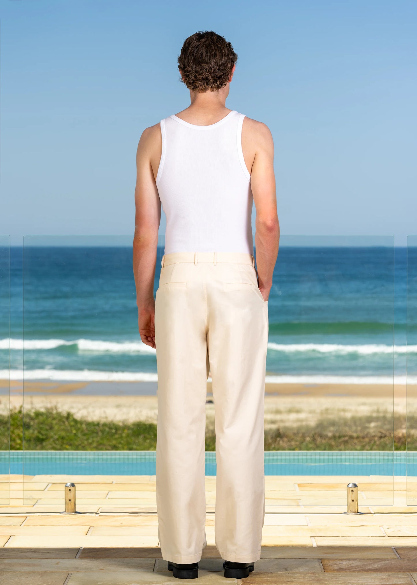 Model shot on location. Beach background, back view of Cream Pleated Pant.