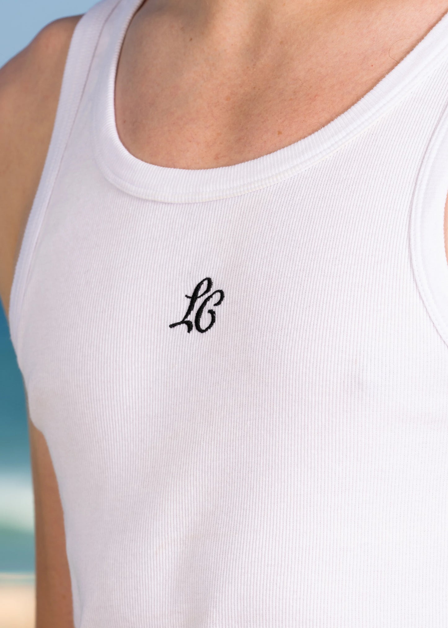 Close-up of model wearing LC monogram embroidered ribbed tank top, scooped neckline.