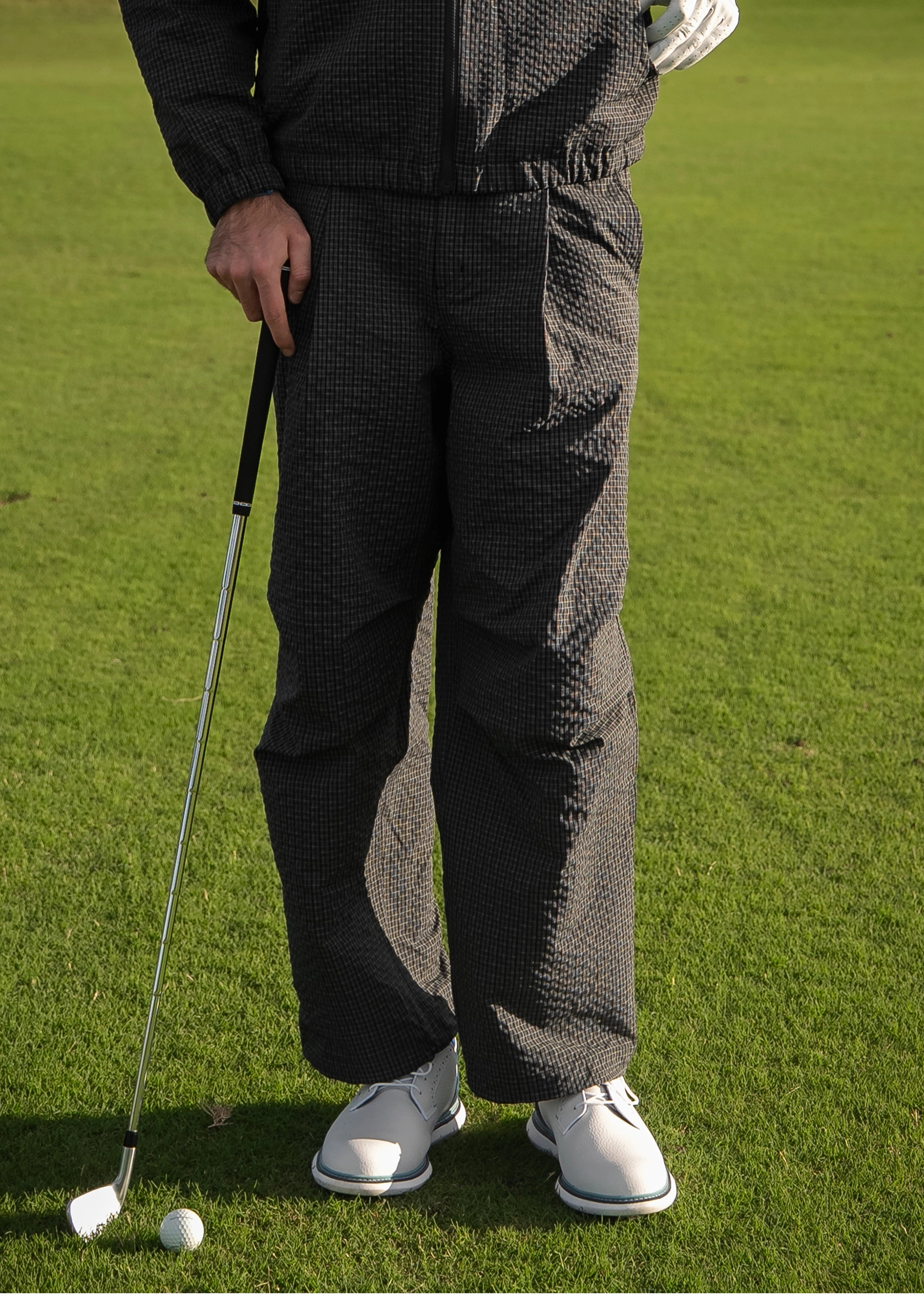 Person on a golf course wearing a navy and black patterned outfit with a golf club and ball.