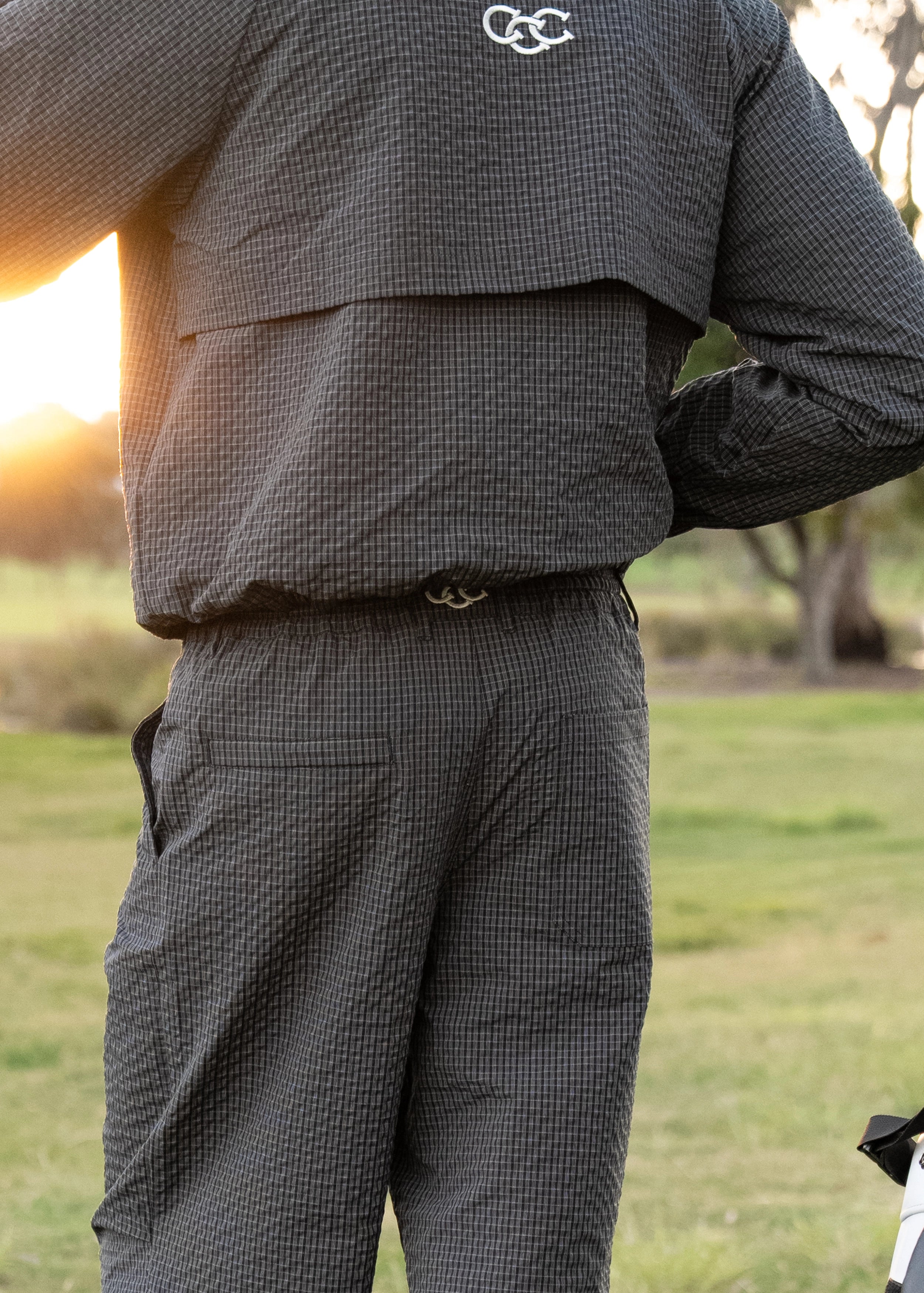 Person wearing a dark checkered jacket and pants in an outdoor setting with a blurred background