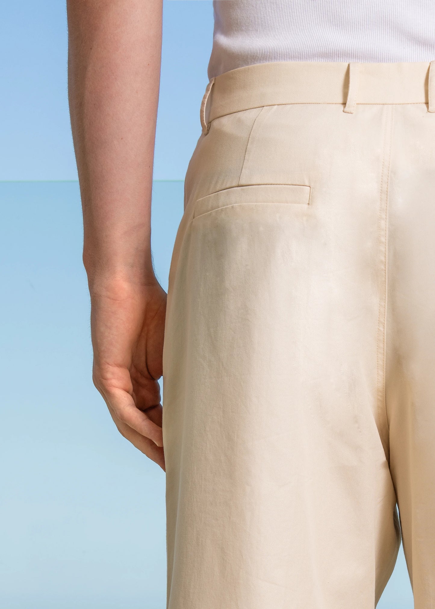 Detailed back view of single welt back pockets with single darts. Reinforced belt loops. Cream Pleated Pant model shot.