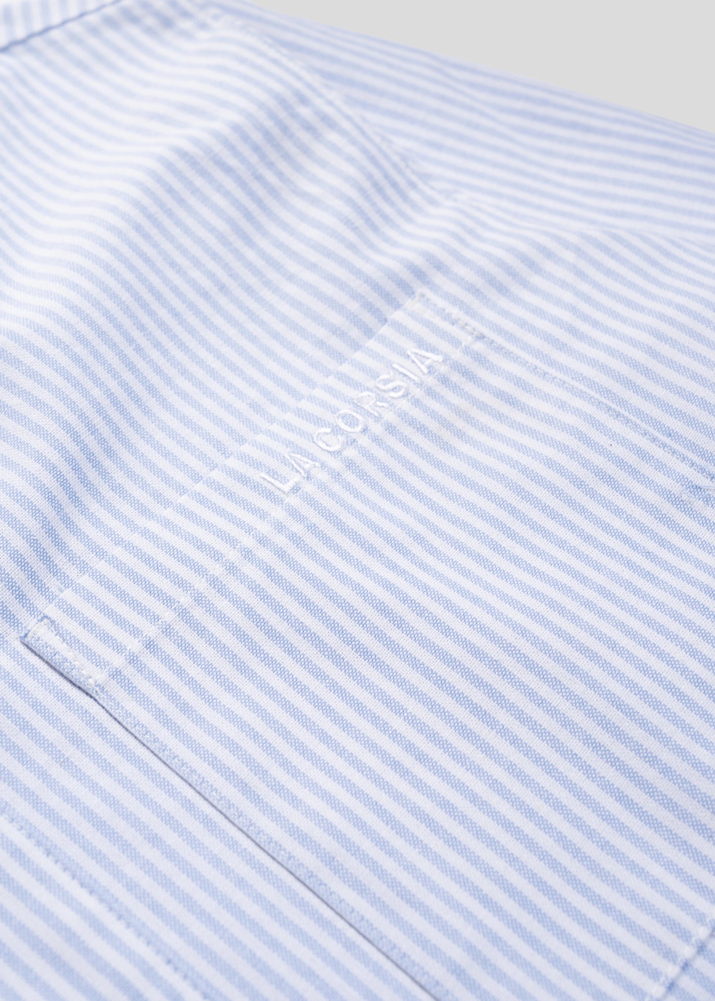 Flatlay closeup showing La Corsia embroidery on front pocket of blue striped business shirt.