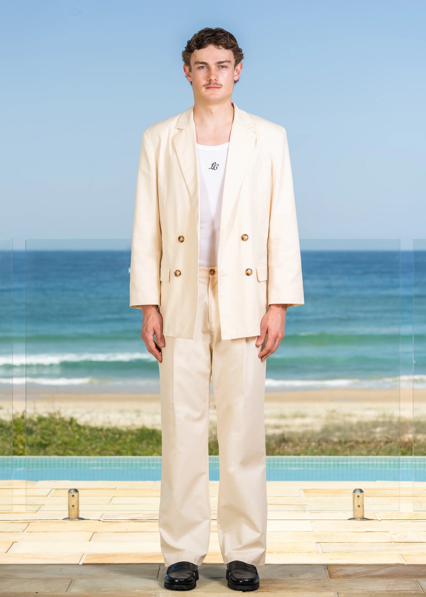 Model shot front view of Double Breasted Jacket with beach background. Unbuttoned closure