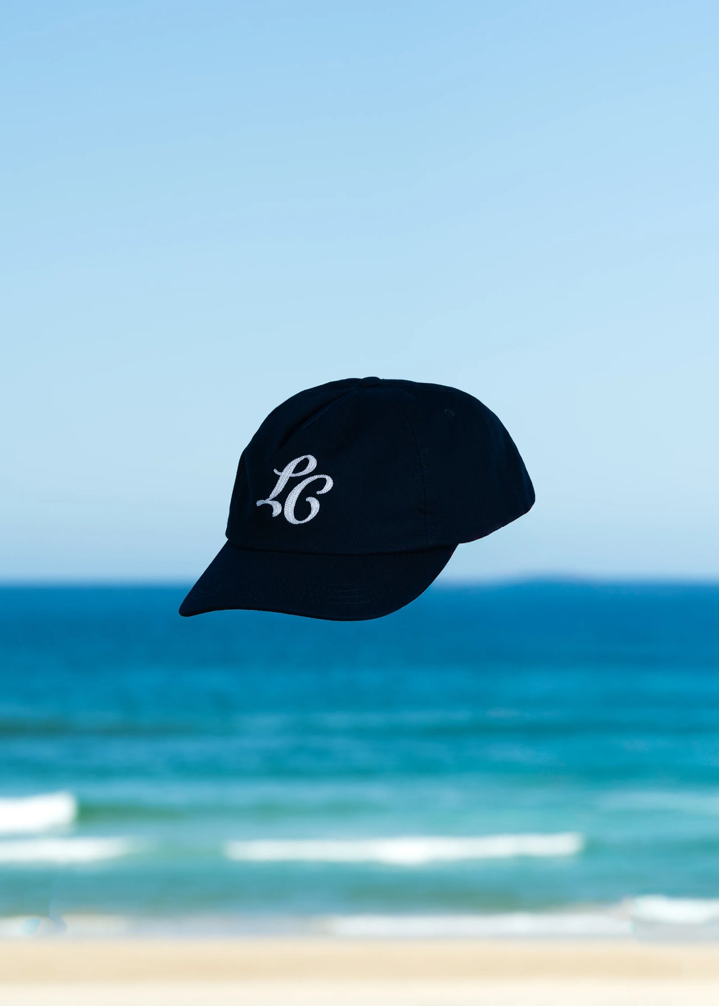 On location Monogram Cap with beach background.