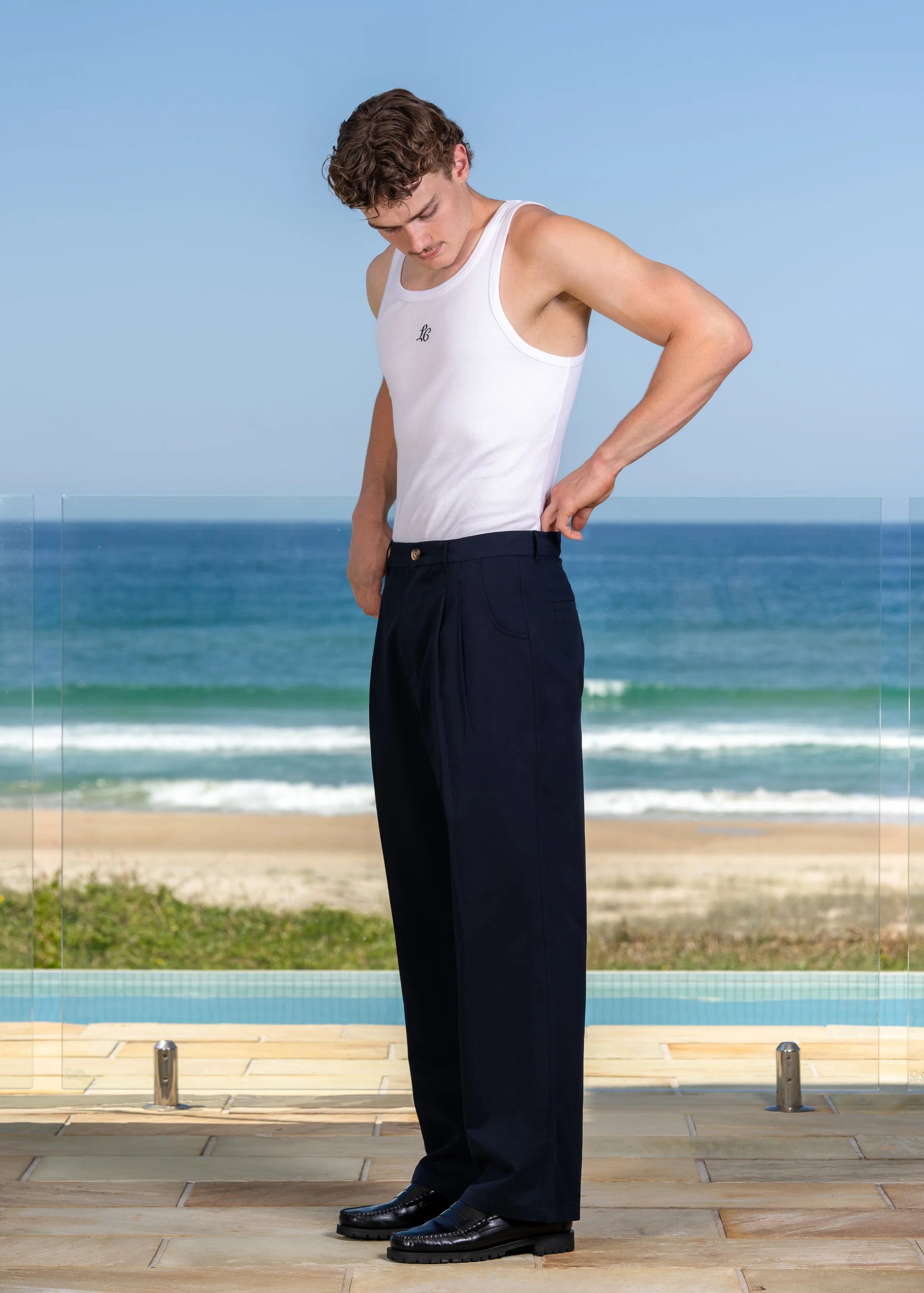 Side view of model wearing white ribbed tank top with LC monogram, casual resort wear by the ocean.