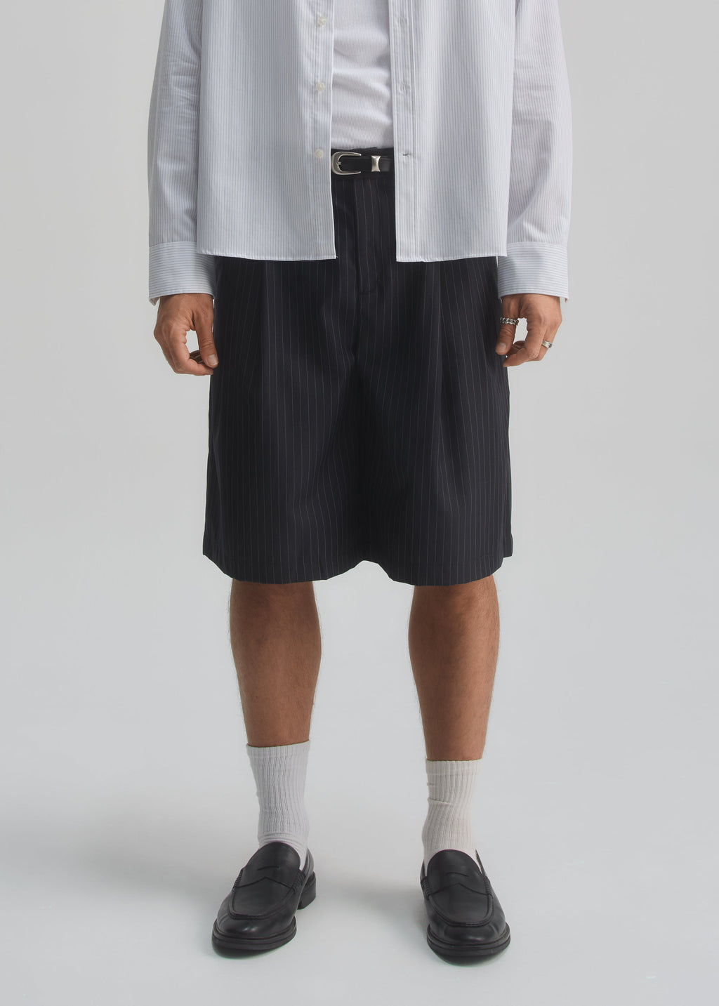 Person wearing a light gray shirt, dark navy pinstripe shorts, white socks, and black shoes on a white background