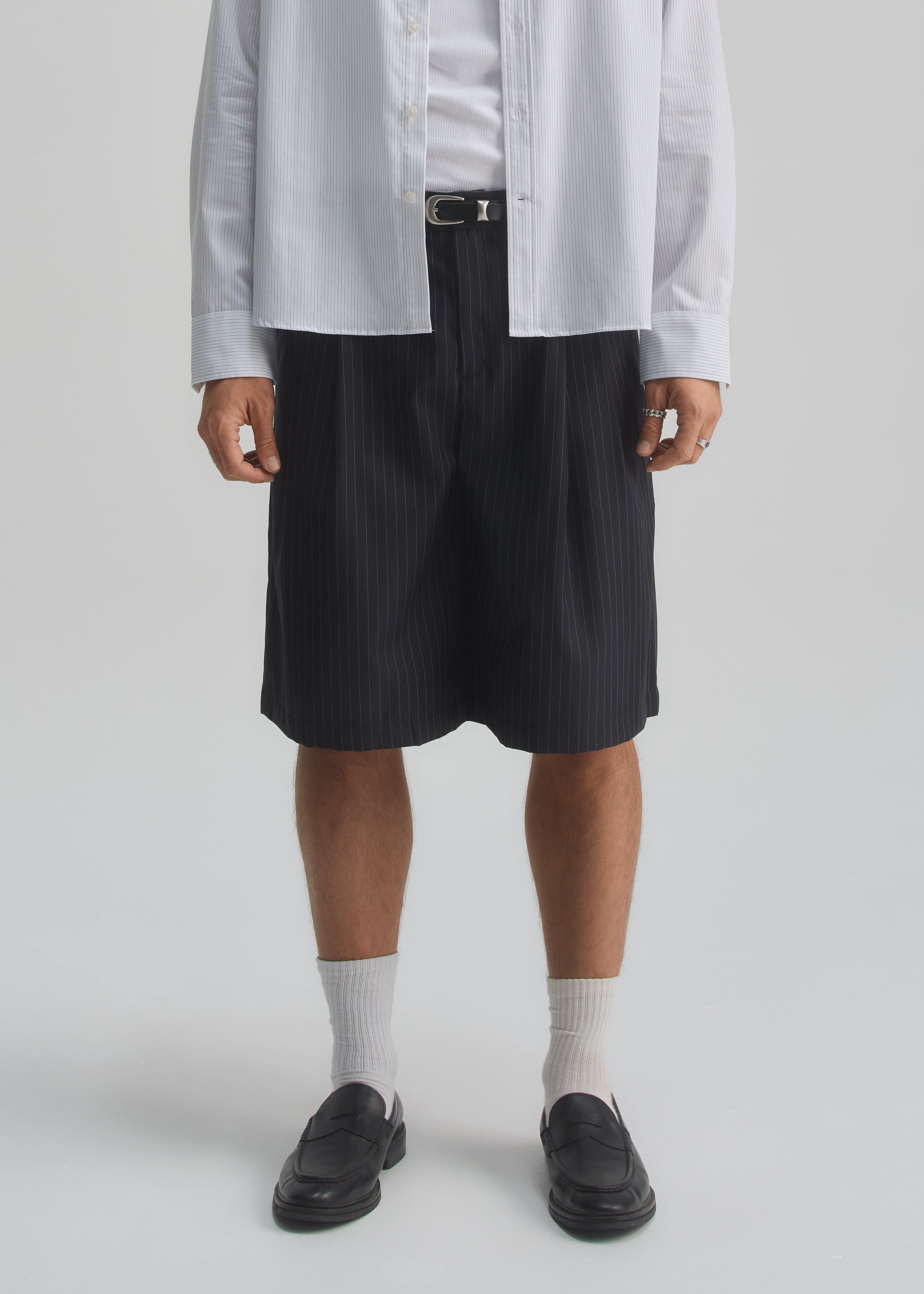 Person wearing a light gray shirt, dark navy pinstripe shorts, white socks, and black shoes on a white background