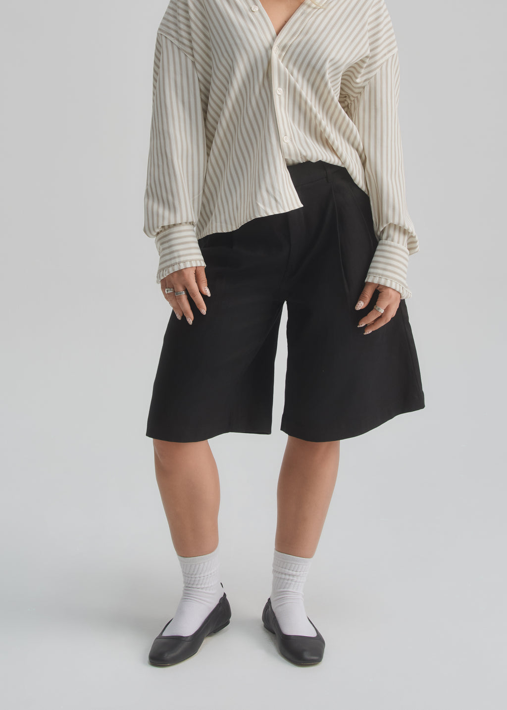 Person wearing a white and gray striped shirt with black shorts on a light gray background