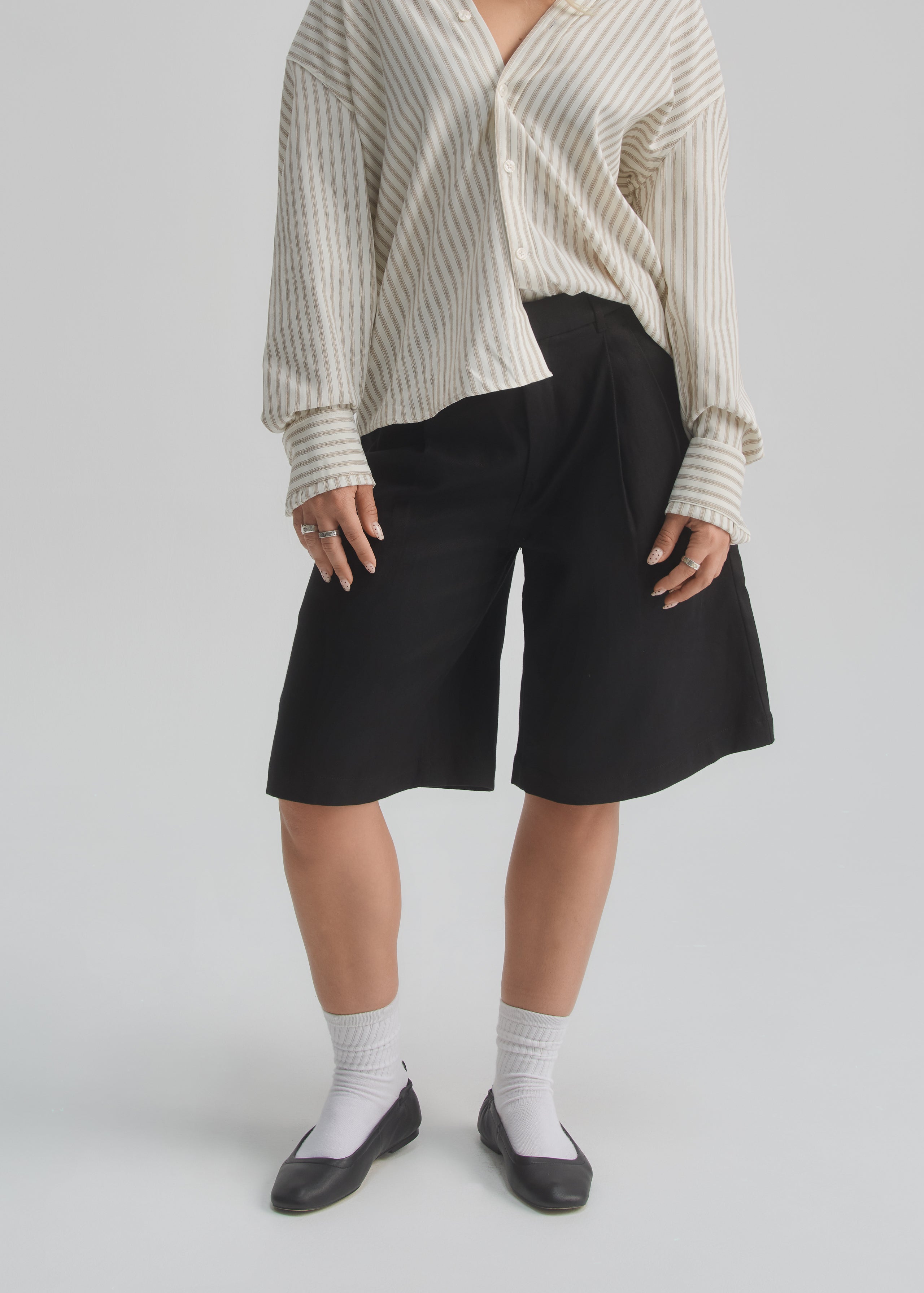 Person wearing a white and gray striped shirt with black shorts on a light gray background