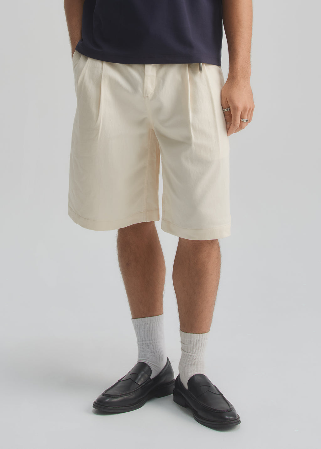 Person wearing beige shorts, black shoes, and white socks on a plain background