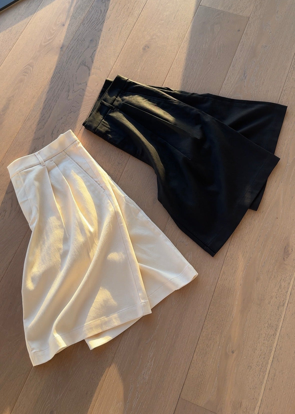Two shorts folded, one cream and one black, on a wooden floor.